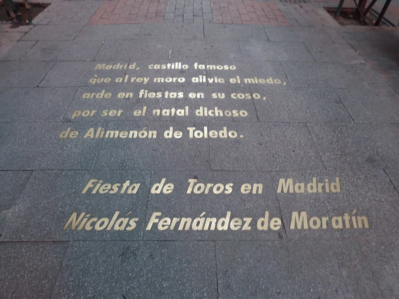 Gold lettering embedded in a dark cobblestone street displaying a Spanish poem by Nicolás Fernández de Moratín
