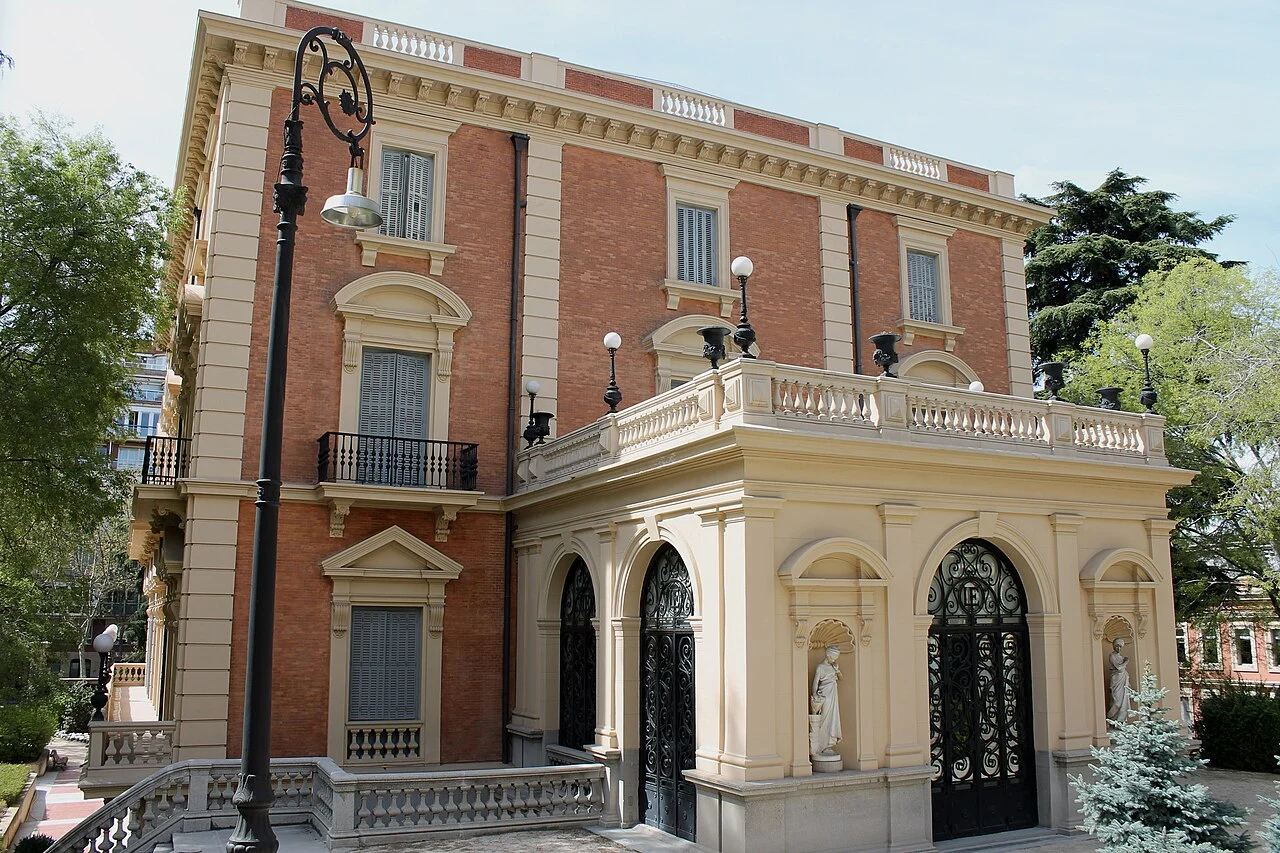 The Museo Lázaro Galdiano featuring a red brick and stone facade, a classical portico with wrought-iron doors, and a vintage street lamp.