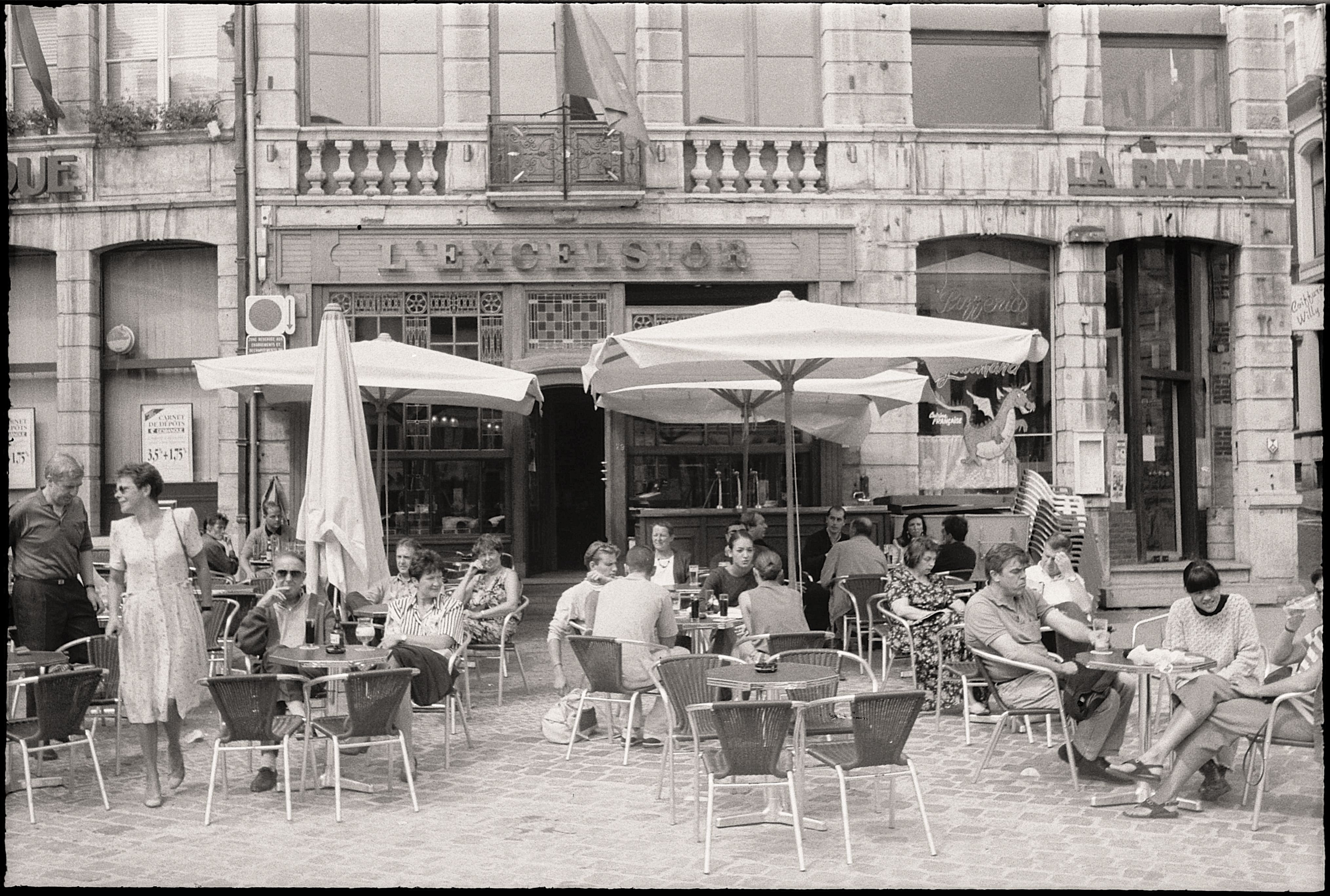 Une photo en noir et blanc d'une terrasse de café avec des gens assis dehors.